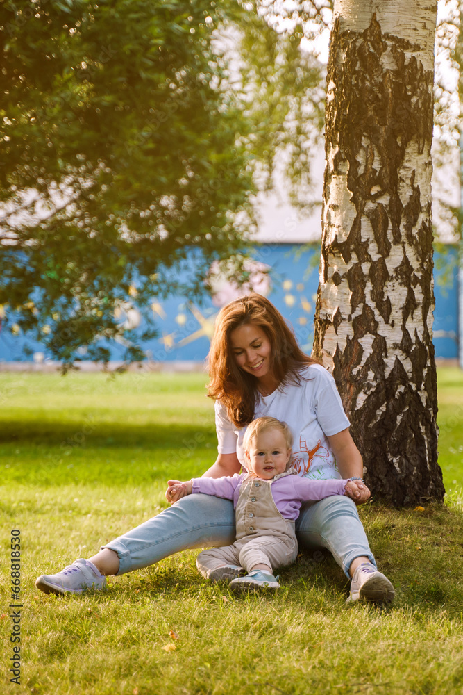 Mother plays with cute blonde baby toddler in the park at sunset. The concept of a happy childhood, a strong family. Sun rays with selective focus Mother plays with cute blonde baby toddler in the park at sunset. The concept of a happy childhood, a strong family. Sun rays with selective focus