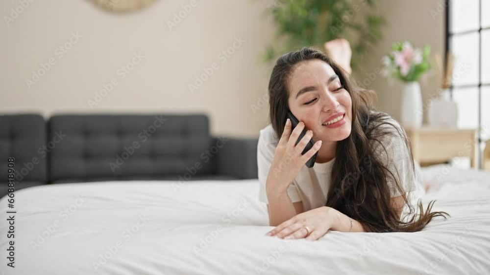Young beautiful hispanic woman talking on smartphone lying on bed smiling at bedroom Young beautiful hispanic woman talking on smartphone lying on bed smiling at bedroom