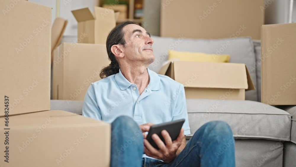 Middle age man using touchpad sitting on floor at new home Middle age man using touchpad sitting on floor at new home