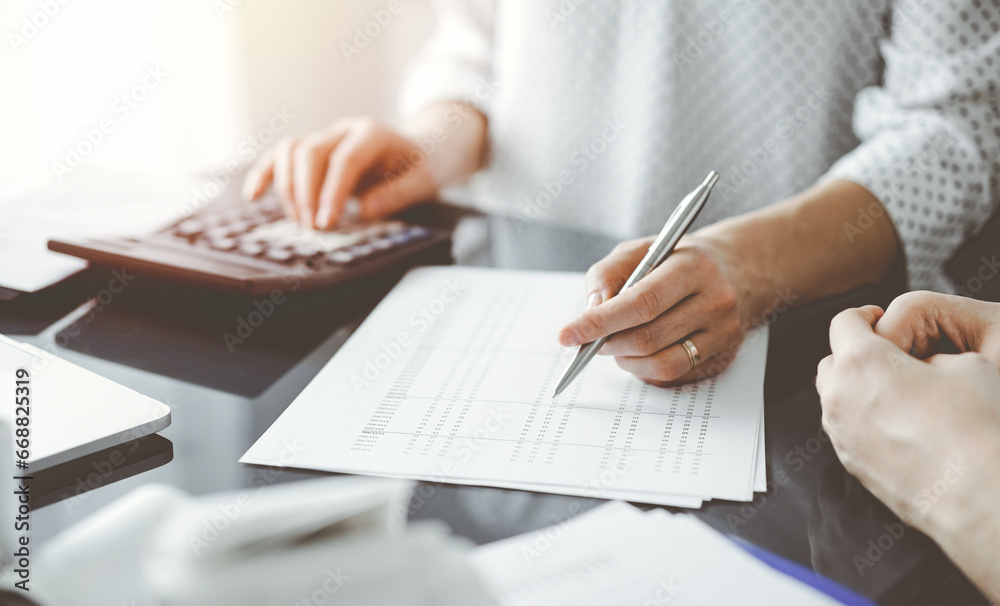 Woman accountant using a calculator and laptop computer while counting taxes for a client. Business audit and finance concepts Woman accountant using a calculator and laptop computer while counting taxes for a client. Business audit and finance concepts