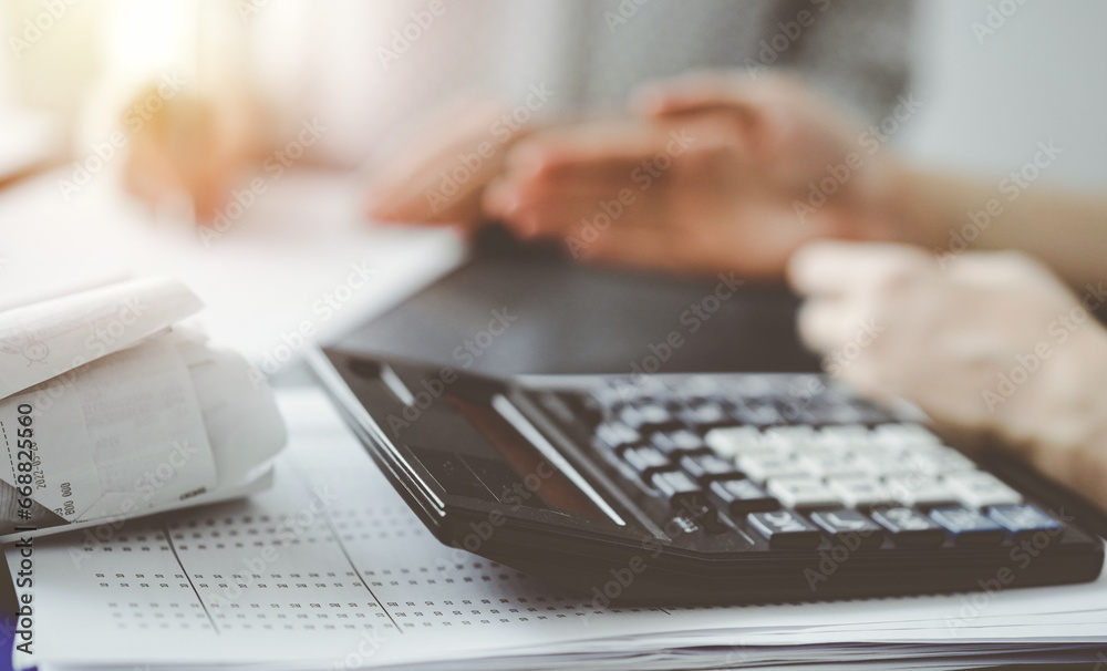 Woman accountant using a pen and laptop computer while counting and discussing taxes with a client, focus on the calculator. Business audit and finance concepts Woman accountant using a pen and laptop computer while counting and discussing taxes with a client, focus on the calculator. Business audit and finance concepts