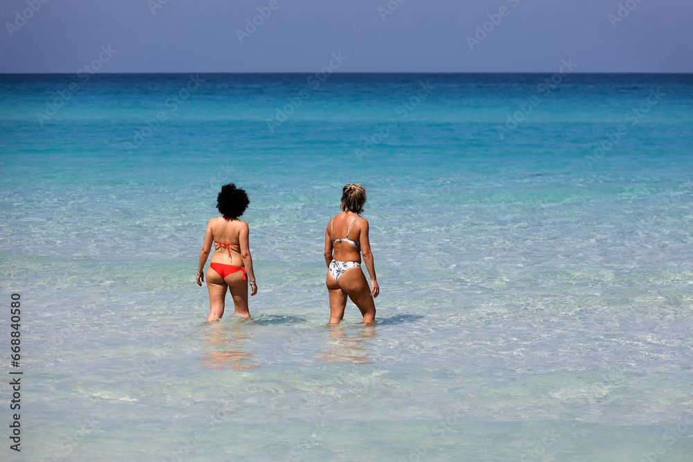 Two women in bikini going to swim in sea water, rear view. Girlfriends on a beach, vacation concept