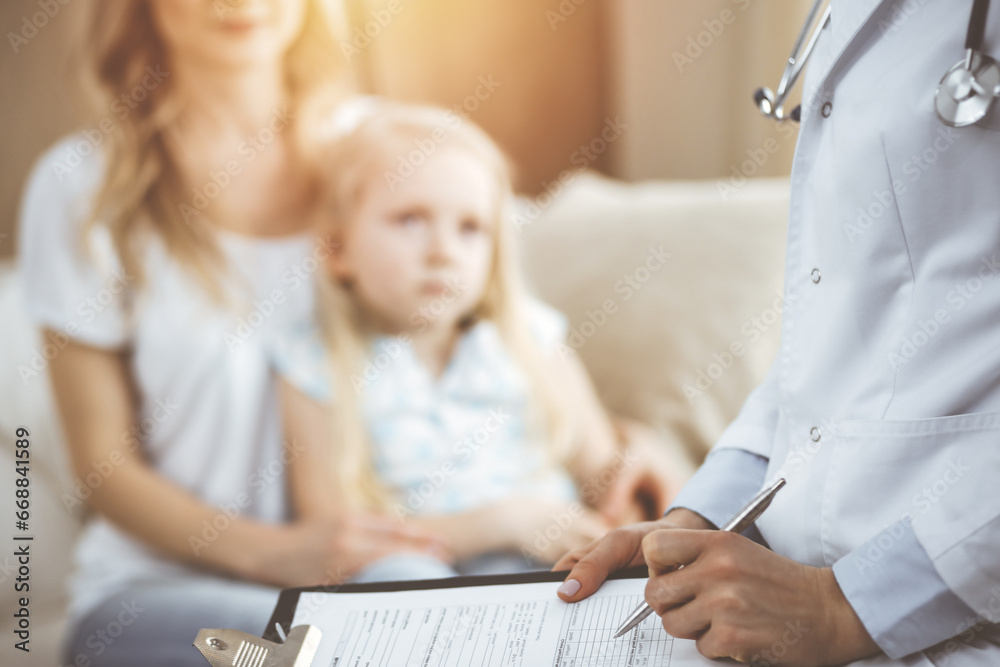 Obraz premium Doctor and patient. Pediatrician using clipboard while examining little girl with her mother at home. Sick and unhappy child at medical exam