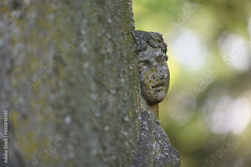 Partial view to a very weathered sandstone sculpture of a female angel face with a gentle look on a cemetery in Weimar-Germany. A female face in front of a blurred, green background. photo