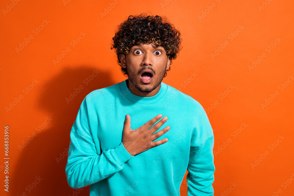 Photo of impressed speechless young man arm touch chest open mouth cant believe isolated on orange color background