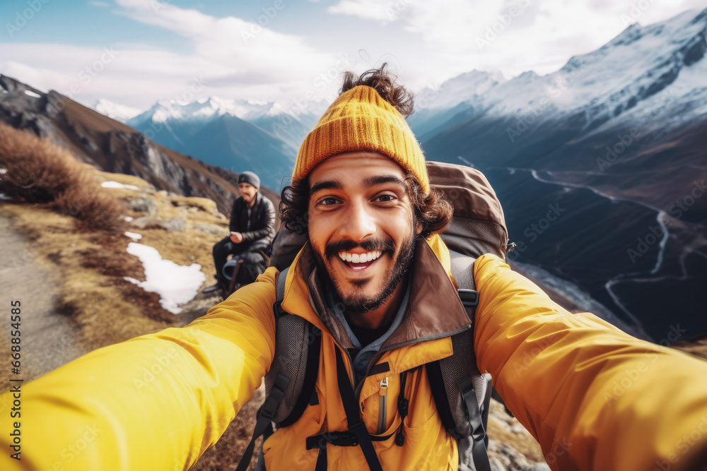 Young indian hiker man taking a selfie portrait on the top of a mountain. Happy young athletic man on an adventure, taking a photo with beautiful view