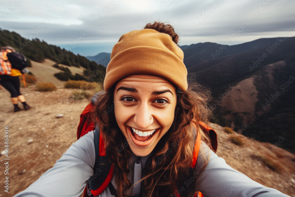 Young latina hiker woman taking a selfie portrait on the top of mountain. Happy young athletic woman on adventure, taking a photo with beautiful view