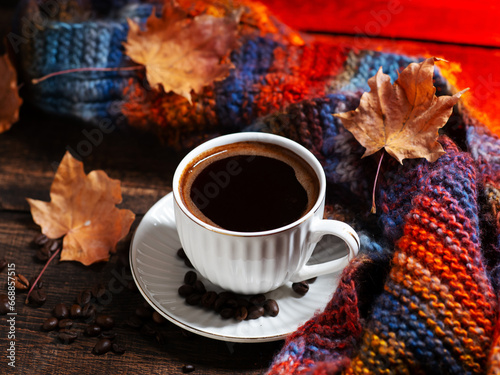 A cup of black coffee on a wooden table. autumn dry maple leaves and knitted scarf. Coffee beans on the table