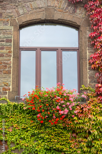 A traditional home window decorated with flowers and covered with leaves around it.