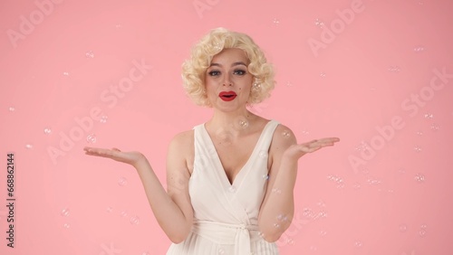 Cheerful beautiful young woman surrounded by soap bubbles. Woman looking like Marilyn Monroe in studio on pink background. Emotions, joy, childhood.