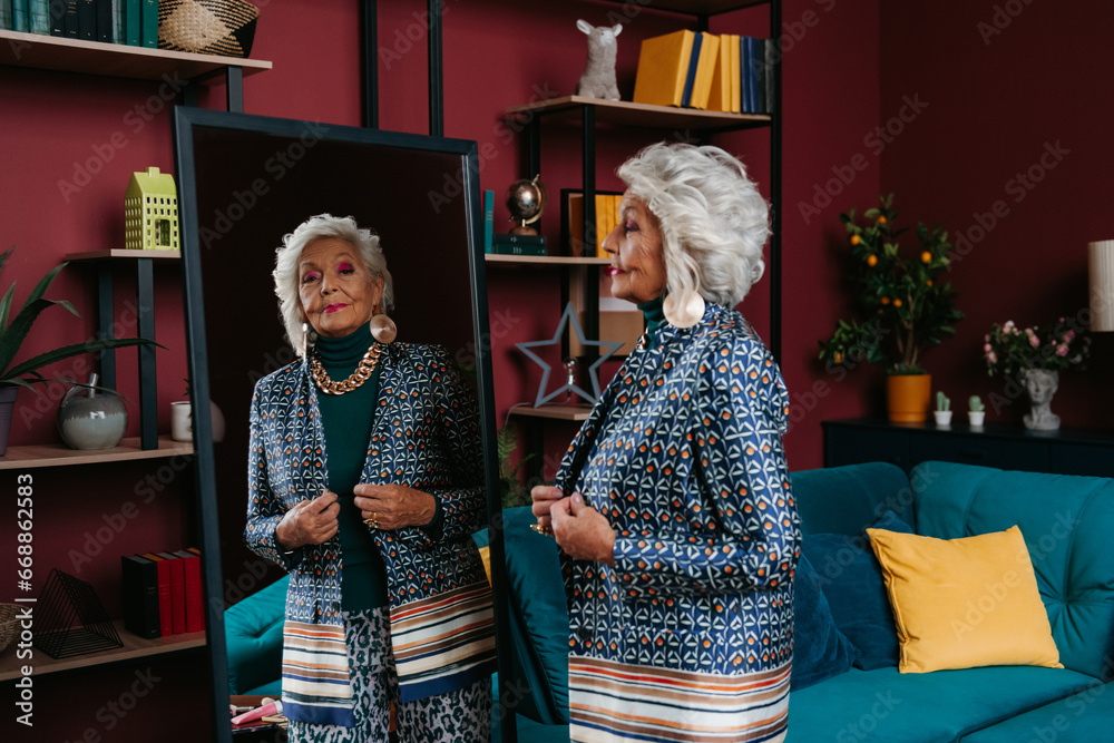 Stylish senior woman trying on fashionable clothes while looking at the mirror at home
