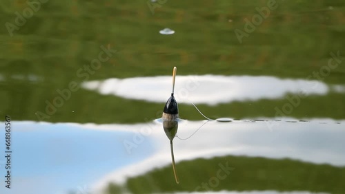 A black and white float on the surface of the lake on a sunny summer day. Fishing tackle made of plastic in the reflection on the surface of the water.