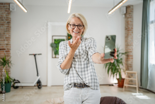 One woman mature caucasian female at home or office use mobile phone hold smartphone take selfie photos self portrait or make a video call daily routine copy space