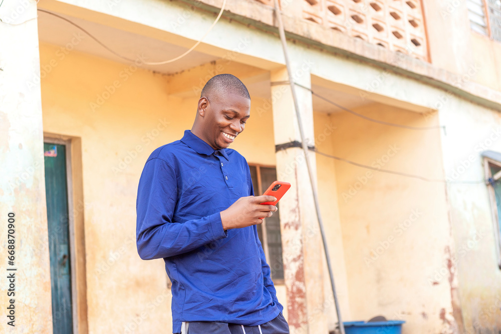 young happy black man standing in front of a building looking at his cell phone