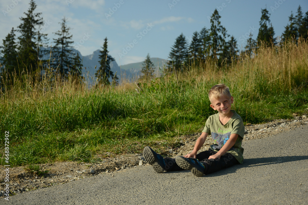 Cute little child, blond, sitting on the road against the backdrop of a mountain landscape