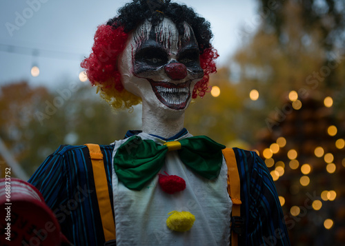 Halloween decoration, grinning clown standing on ghosts background in the forest