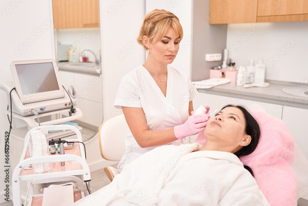 Esthetician applies cream to a woman face with an applicator Esthetician applies cream to a woman face with an applicator