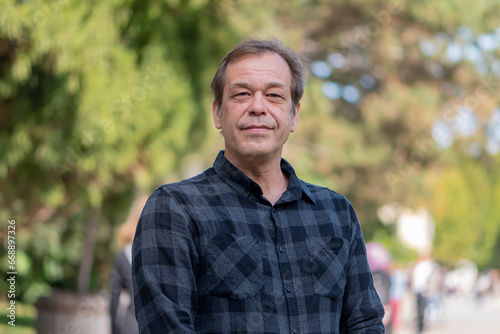 Portrait of a confident man of 45-50 years old on a neutral blurred background of a city park.