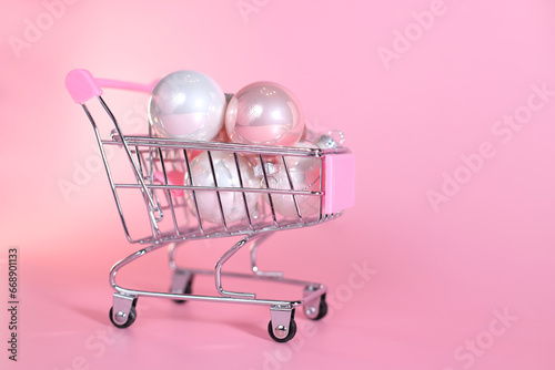 Shopping basket trelley with Christmas tree balls decoration on pink background