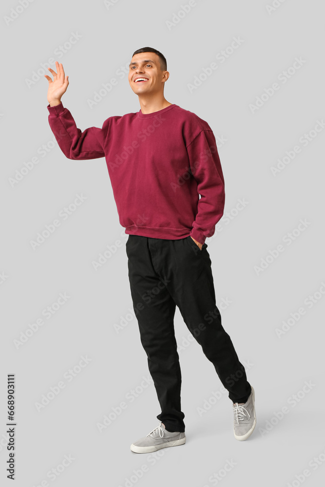 Handsome young man waving hand on grey background Handsome young man waving hand on grey background