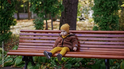 Beautiful toddler boy sits on the bench waving his foot. Calm baby boy resting in the park. photo