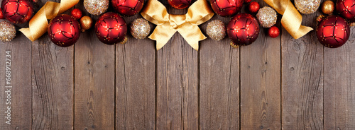 Christmas top border of red and gold ornaments and ribbon. Overhead view on a dark wood banner background. Copy space.
