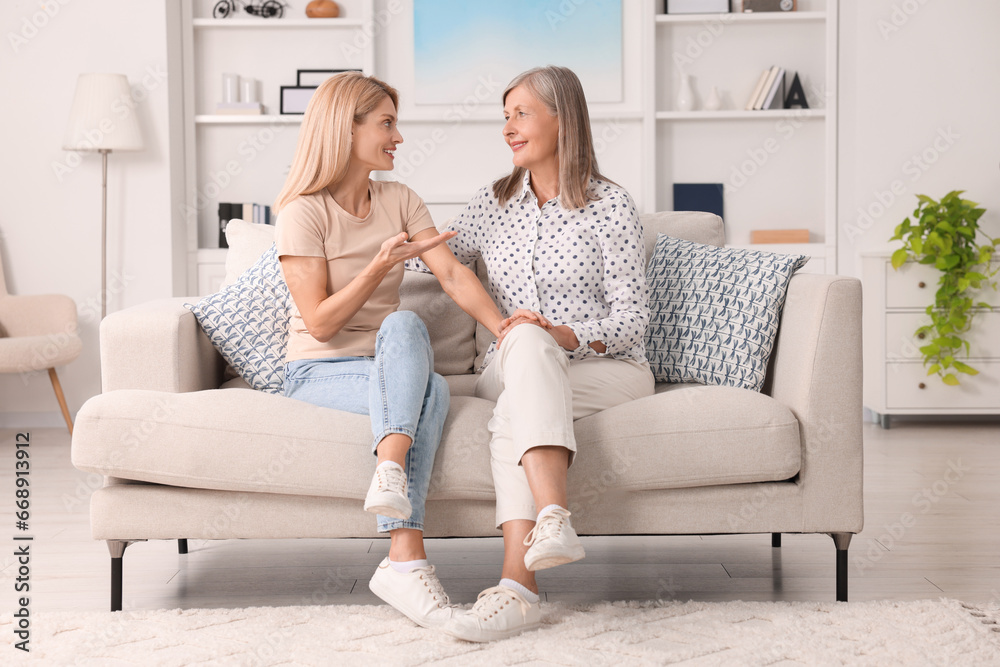 Happy mature mother and her daughter talking on sofa at home Happy mature mother and her daughter talking on sofa at home