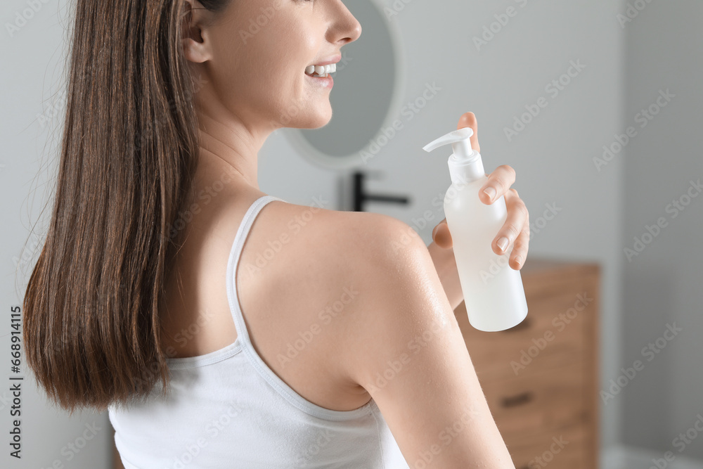 Woman applying body oil onto shoulder in bathroom, closeup Woman applying body oil onto shoulder in bathroom, closeup