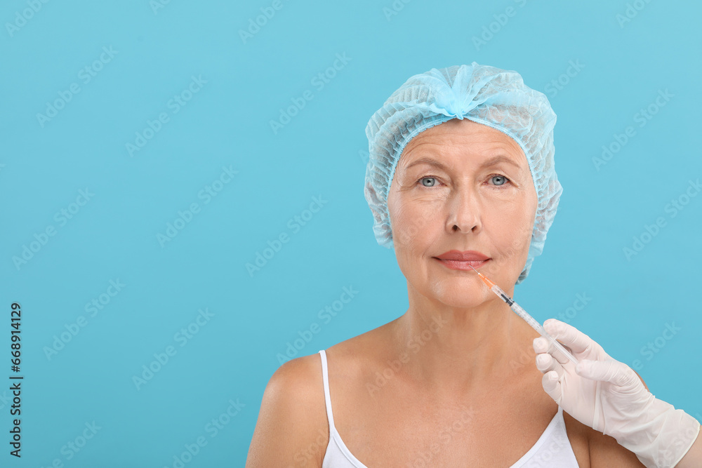 Doctor giving lips injection to senior woman on light blue background, space for text. Cosmetic surgery Doctor giving lips injection to senior woman on light blue background, space for text. Cosmetic surgery