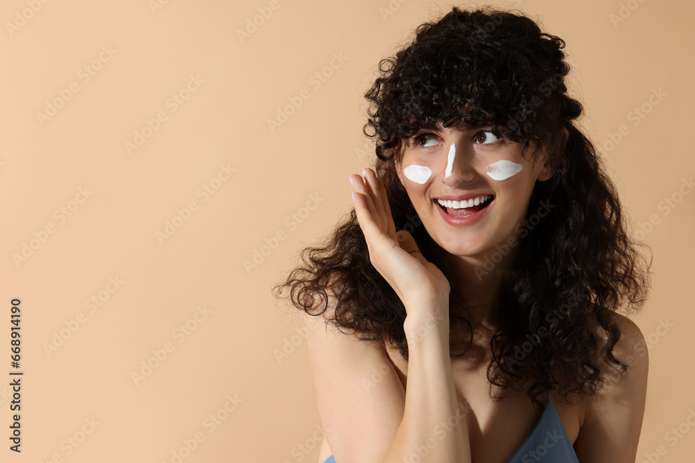 Beautiful young woman with sun protection cream on her face against beige background, space for text Beautiful young woman with sun protection cream on her face against beige background, space for text