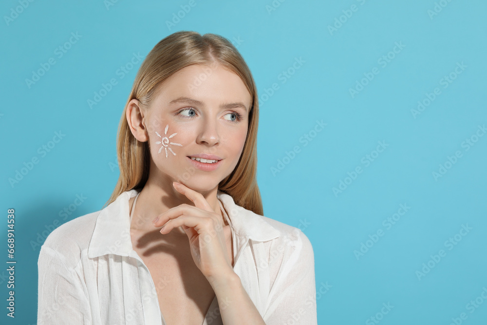 Beautiful young woman with sun protection cream on her face against light blue background, space for text