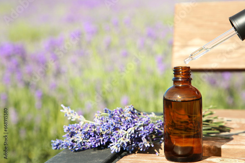 Dripping essential oil from pipette into bottle near lavender on wooden table outdoors  closeup. Space for text