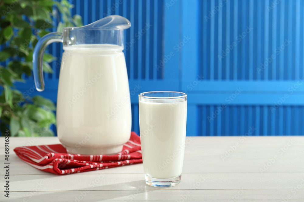 Jug and glass of fresh milk on white wooden table, space for text Jug and glass of fresh milk on white wooden table, space for text