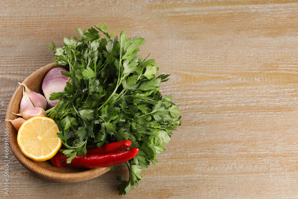 Bowl with fresh green parsley, chili peppers, lemon, onion and garlic on wooden table, above view. Space for text Bowl with fresh green parsley, chili peppers, lemon, onion and garlic on wooden table, above view. Space for text
