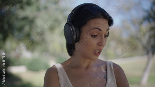 smiling young woman talking on the phone through her headset while strolling through a park in her home town