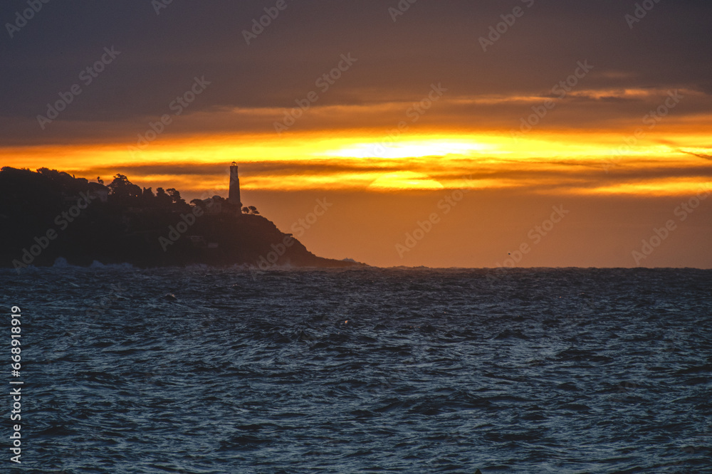Lever de soleil sur la mer à Nice sur la Côte d'Azur avec des lueurs dorées sur le phare du Cap Ferrat