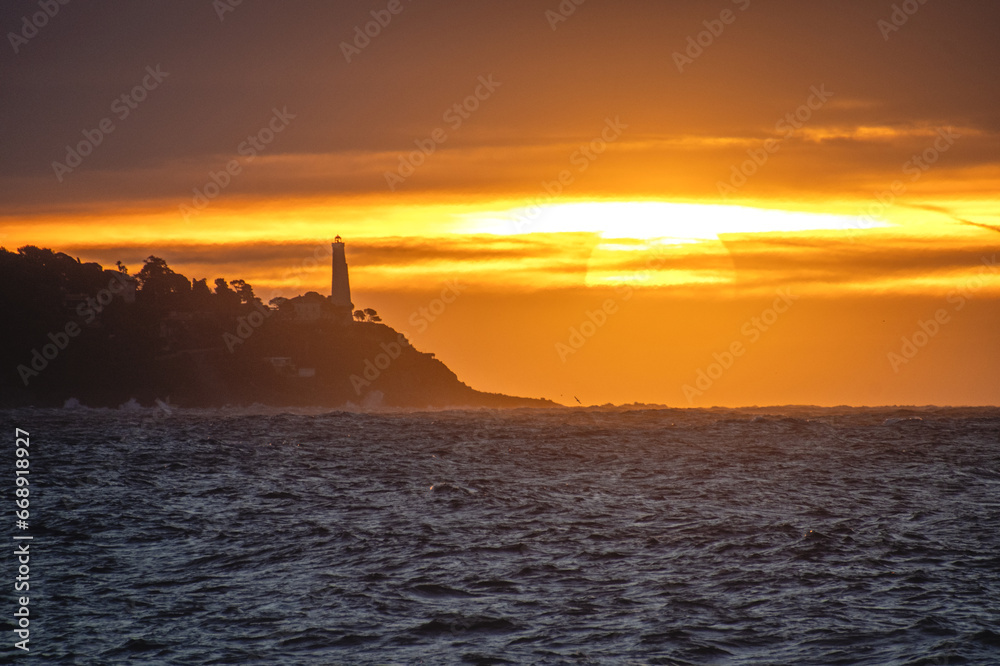 Lever de soleil sur la mer à Nice sur la Côte d'Azur avec des lueurs dorées sur le phare du Cap Ferrat Lever de soleil sur la mer à Nice sur la Côte d'Azur avec des lueurs dorées sur le phare du Cap Ferrat