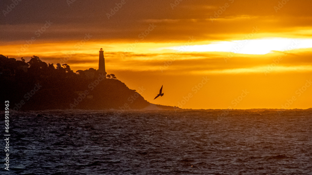 Lever de soleil sur la mer à Nice sur la Côte d'Azur avec des lueurs dorées sur le phare du Cap Ferrat