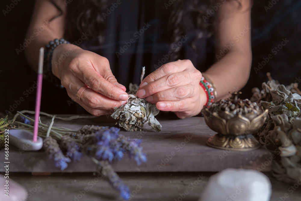 woman doing traditional ritual with herbs tying them with cotton thread accompanied by incense woman doing traditional ritual with herbs tying them with cotton thread accompanied by incense