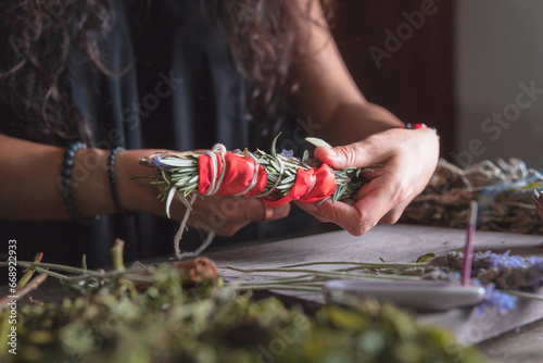 woman doing traditional ritual with herbs tying them with cotton thread accompanied by incense