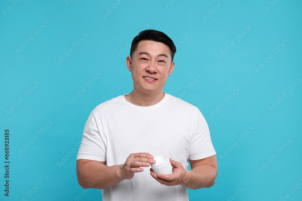 Handsome man with jar of body cream on light blue background Handsome man with jar of body cream on light blue background