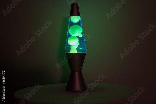 Green and blue lava lamp stands near a white wall in the darkness photo