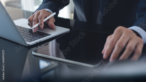 Businessman, project manager working on laptop computer, using digital tablet planning work project at modern office. Business man searching, analyzing business data, surfing the internet on laptop