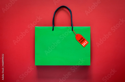 Green shopping paper bag with word at price tag on red background for Black Friday shopping sale concept.