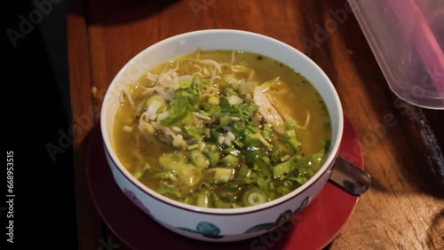 The video features a delicious bowl of Soto Ayam, an Indonesian chicken soup with aromatic spices, tender chicken, and rice noodles. It's garnished with fresh herbs, crispy shallots, and lime