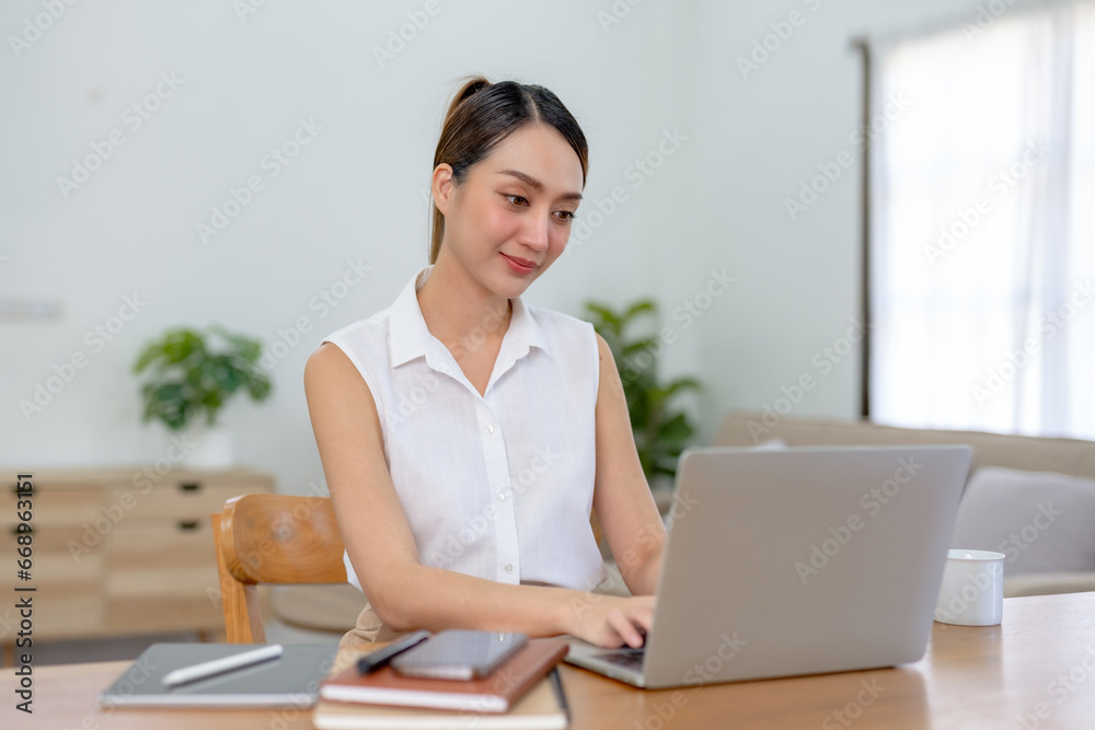 Obraz premium Happy asian woman using laptop while working remotely from home in living room.