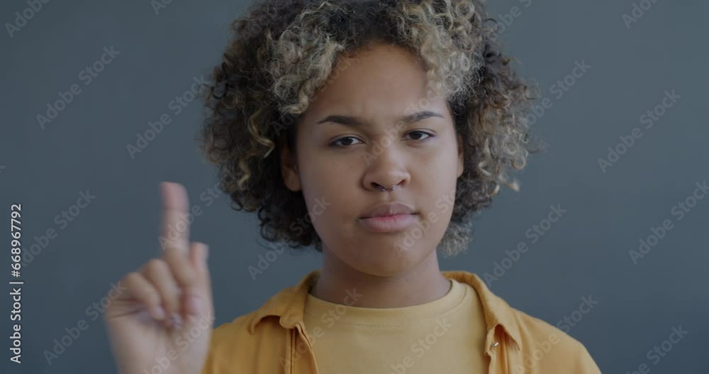 Close-up slow motion portrait of strict African American lady shaking head and wagging finger on gray background. Body language and people concept. Close-up slow motion portrait of strict African American lady shaking head and wagging finger on gray background. Body language and people concept.