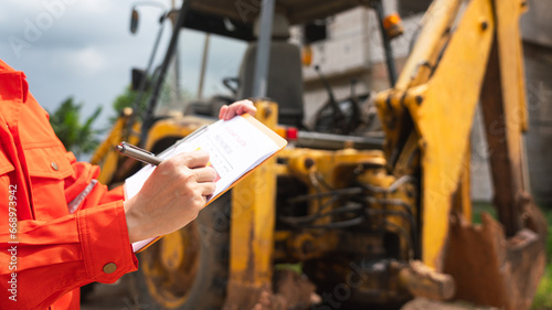 Konstfotografi A mechanical engineer is using checklist form to verify the excavator or earthmover machine (as background) condition before operating at construction site