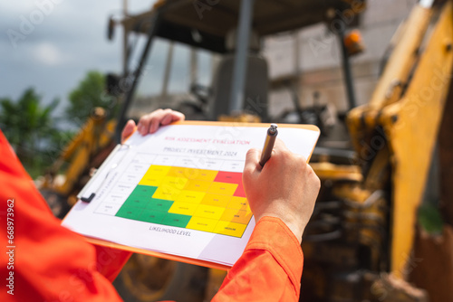 The operation supervisor is using ballpoint pen to marking on the risk assessment matrix form, to inspection the backhoe machine that using at construction worksite.