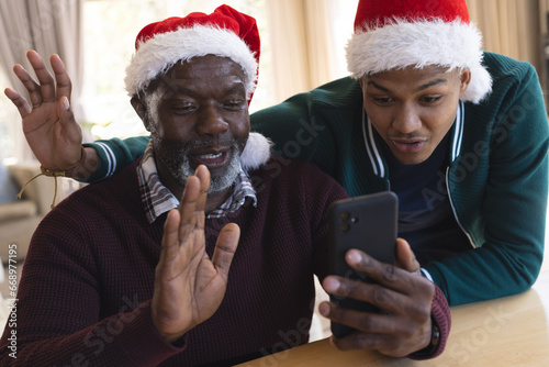 Happy african american father and son in christmas hats having smartphone video call